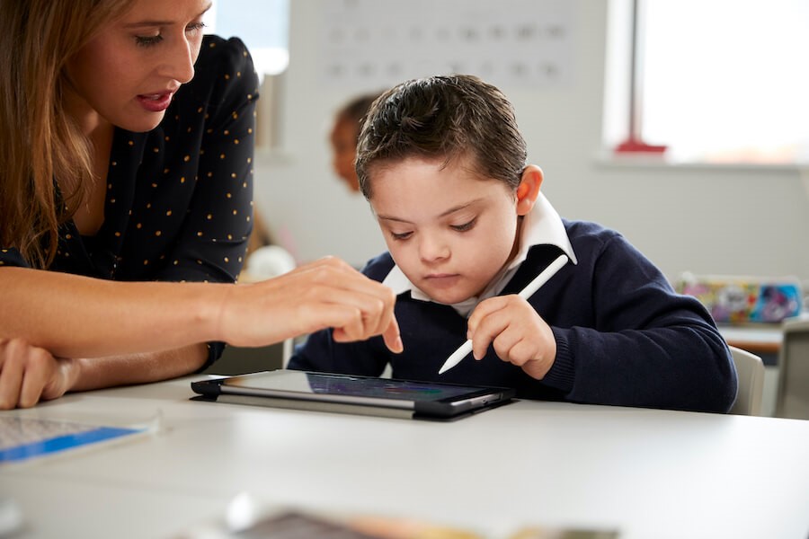 Student with down syndrome using an ipad with assistance from a female teacher