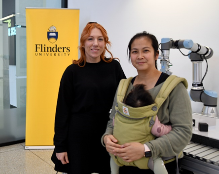 Image of two women standing. One of the two women is holding a baby.