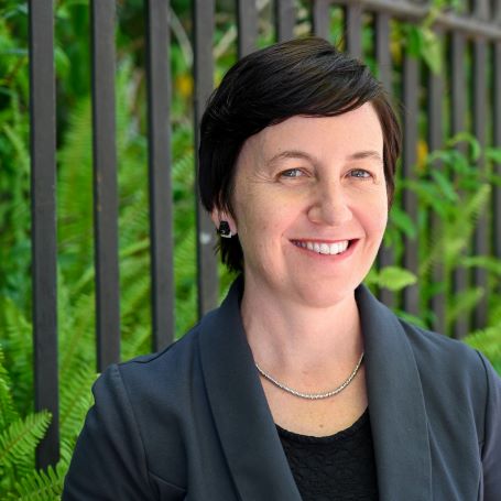 Dr Jordana Hunter head shot of woman smiling with dark short hair wearing a grey suit jacket and black tshirt