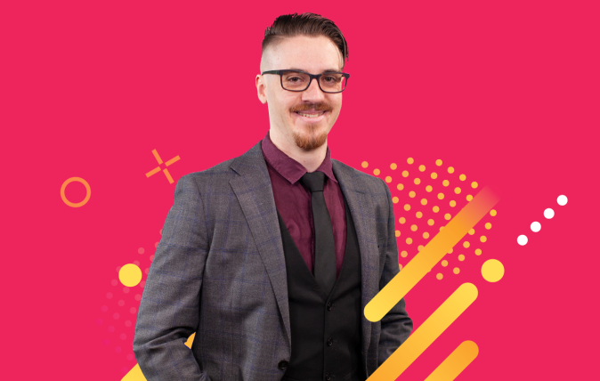 photo of Elijah smiling wearing business clothes standing in front of a pink background