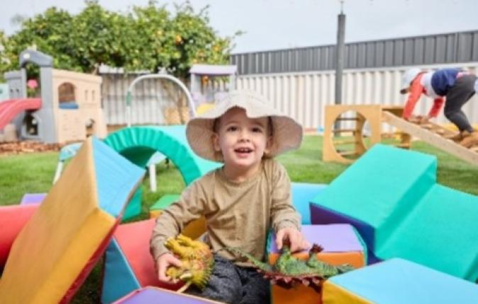 Young boy playing wearing a hat outdoors at a child care centre among soft equipment